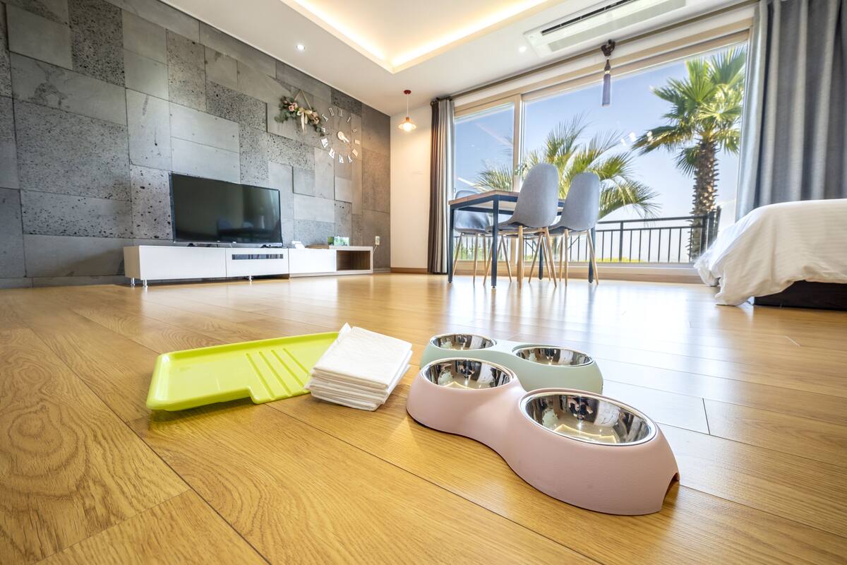 A modern living room with a flat-screen TV, pet bowls, and a dining area with chairs.
