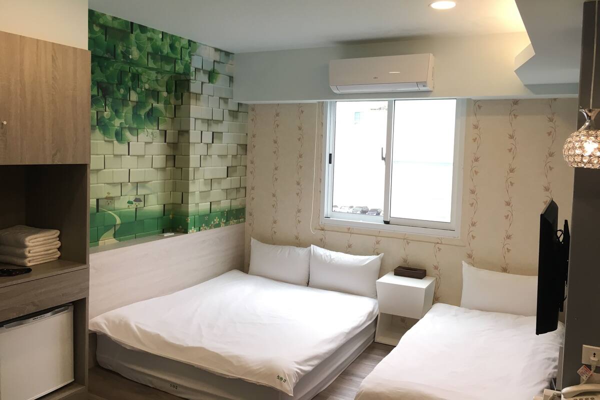 Ein Hotelzimmer mit Bett, Nachttisch, Kleiderschrank, Wandklimaanlage und Fenster mit Aussicht.