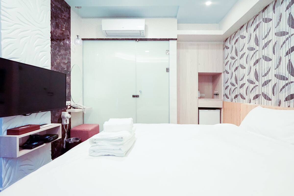 Ein Hotelzimmer mit Bett, Fernseher, Schreibtisch mit Computer und einem Badezimmer mit Dusche.