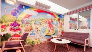 Ein Spielzimmer für Kinder mit Wandgemälde in bunten Farben, einer Couch, einem kleinen Tisch und einem Stuhl.