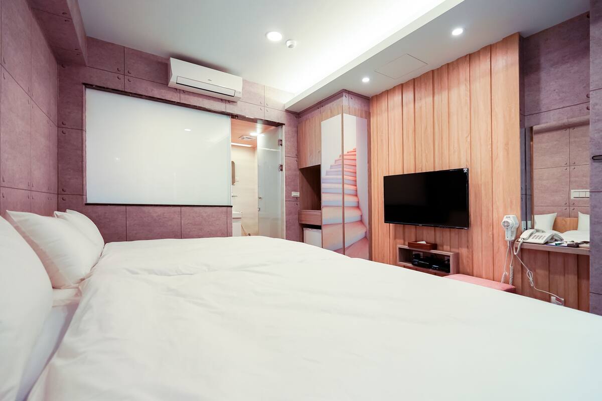 Ein modernes Hotelzimmer mit einem großen Bett, einem flachbildfernseher an der Wand, einem fest installierten Föhn und Wandverkleidung aus Holz.