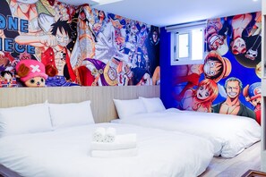 Quarto de hotel com um grande mural de One Piece na parede, uma cama com roupa de cama branca e uma janela.