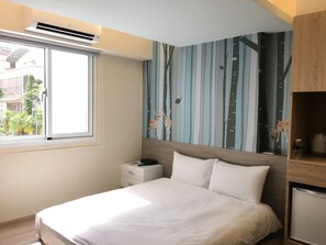 Quarto de hotel moderno com uma cama grande, uma mesinha de cabeceira, um mini-frigorífico embutido e uma janela com vista para o exterior.