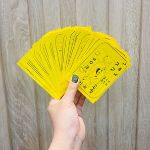 Mão segurando um leque amarelo com um personagem de desenho animado e texto.