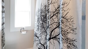 Un baño con inodoro blanco, una ventana y cortina de ducha con diseño de árbol.