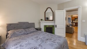 Un dormitorio con cama, mesita de noche, espejo y chimenea.
