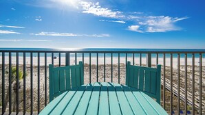 Vista de la playa desde un balcón con una silla verde y barandilla.