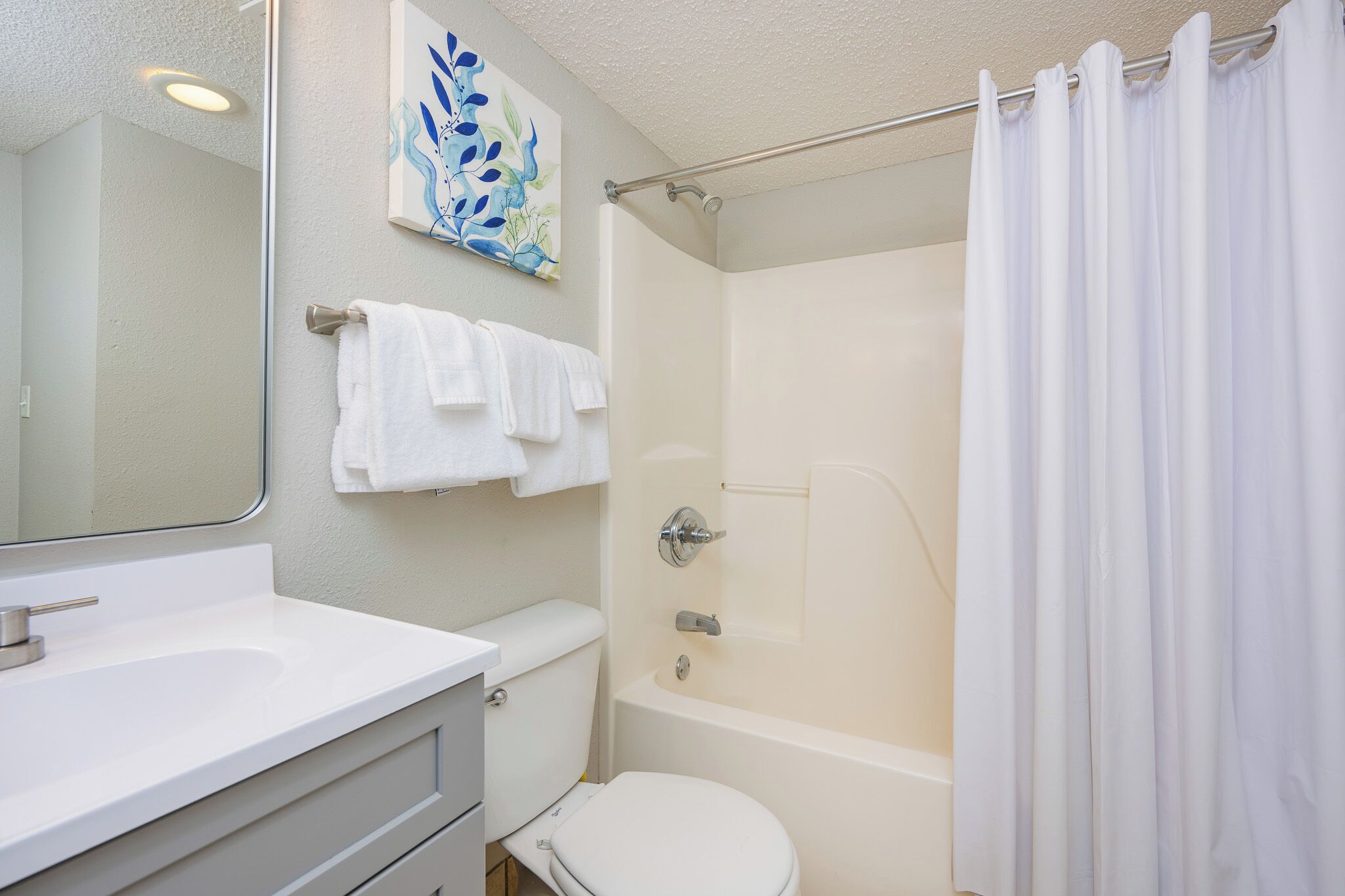 Une salle de bain avec un lavabo, des toilettes et une douche, tous de couleur blanche. On y trouve un porte-serviettes avec plusieurs serviettes et un rideau de douche.