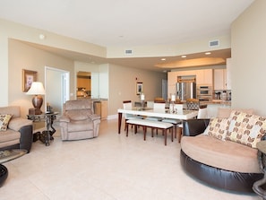A spacious living room with a dining area, a kitchen in the background, and a large window providing natural light.