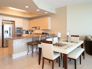 A modern kitchen with a central island, built-in appliances, and a dining area with a glass-top table and chairs.
