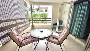 Une table ronde en verre, entourée de quatre chaises à coussins rayés, dans un espace balcon.