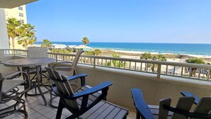A balcony with a view of the beach, equipped with chairs and a table.
