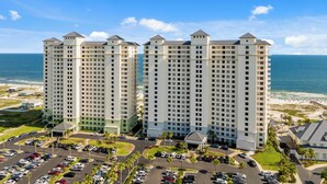 A high-rise hotel with multiple floors, a parking lot, and a beach view.