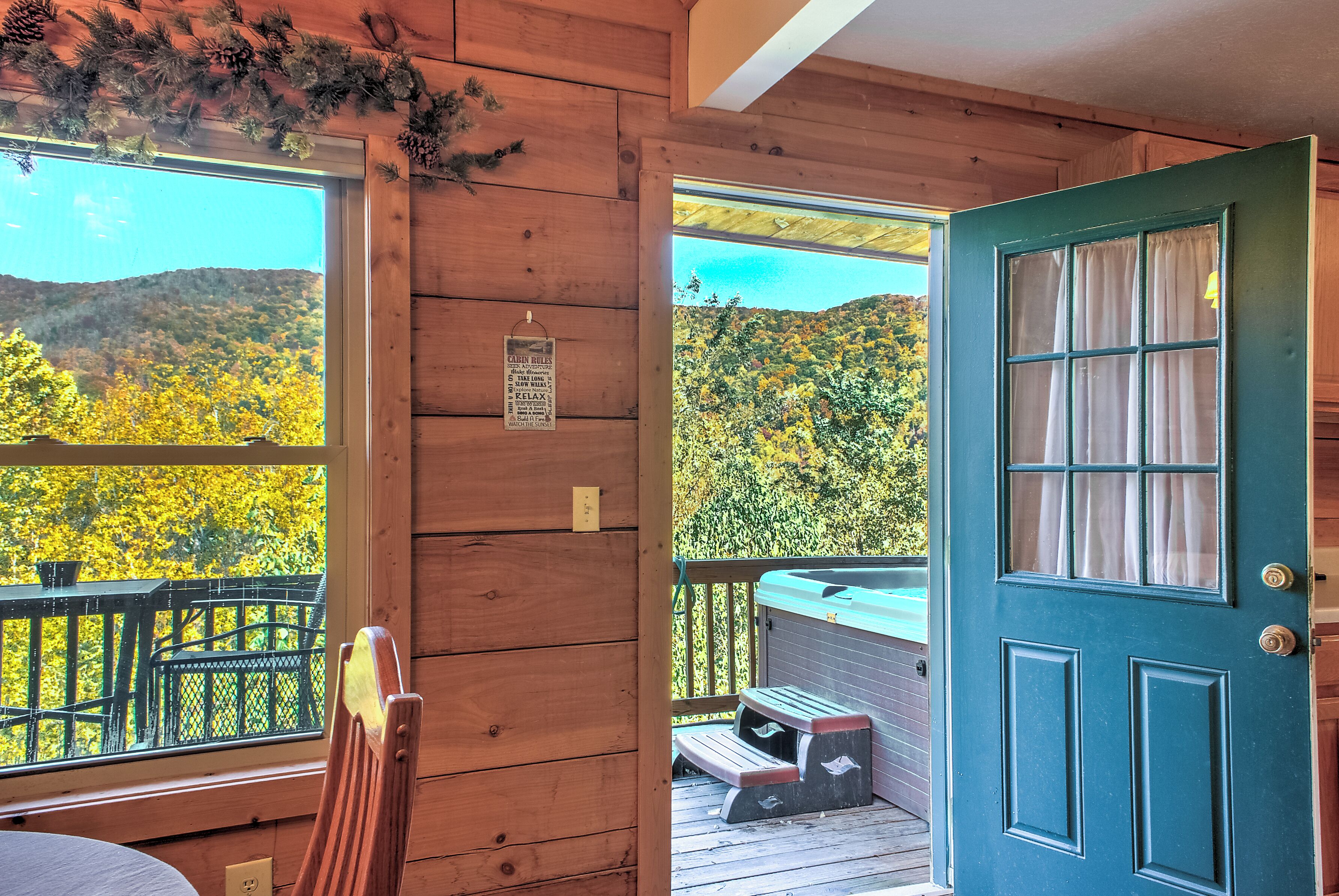 A wooden cabin with a view of autumn foliage, a wooden deck, and a hot tub.