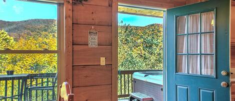 A wooden cabin with a view of autumn foliage, a wooden deck, and a hot tub.