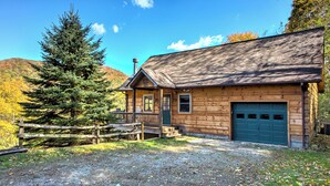 A wooden cabin with a green door, a covered porch, and a garage. - Pet-Friendly Modern Cabin w/ Hot Tub, Mountain Views + Biltmore Pass (Waynesville)