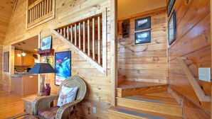 L’intérieur d’un chalet en bois, avec un escalier, des meubles en osier et un téléviseur.