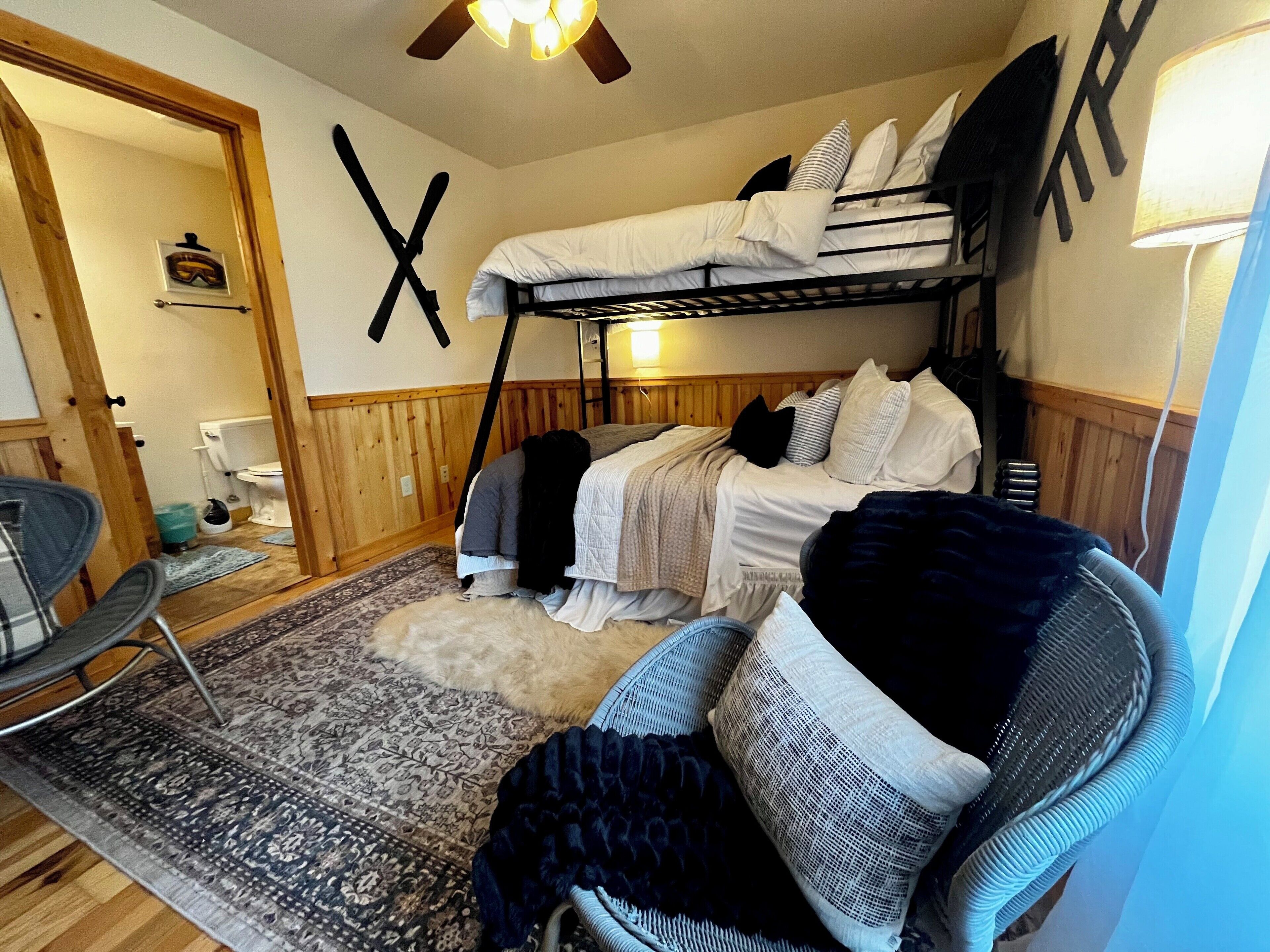 Una stanza piccola con un letto a castello, una sedia, un tappeto e un pannello di legno decorato con una 'T'.