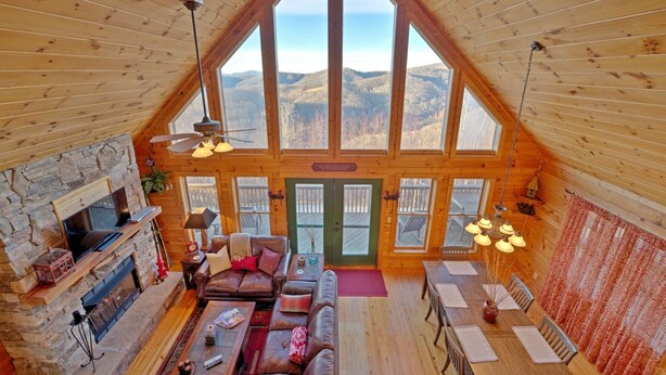Un vaste espace de vie aménagé dans un style industriel, avec une cheminée en pierre, un canapé en cuir, une table à manger et de grandes fenêtres offrant une vue sur les montagnes.