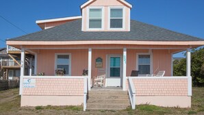 A single-story house with a gabled roof, a front porch with a swing chair, and a brick facade. - Hunnicutt House: Oceanfront 4BR-Short Walk to Kure Beach Pier (Kure Beach)