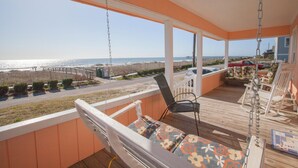 A covered outdoor area with a swing chair, a cushioned bench, and a view of the beach and ocean. - Hunnicutt House: Oceanfront 4BR-Short Walk to Kure Beach Pier (Kure Beach)