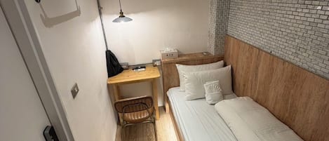 A compact room with a bed, a desk, a chair, an air conditioning unit, and a hanging lamp.