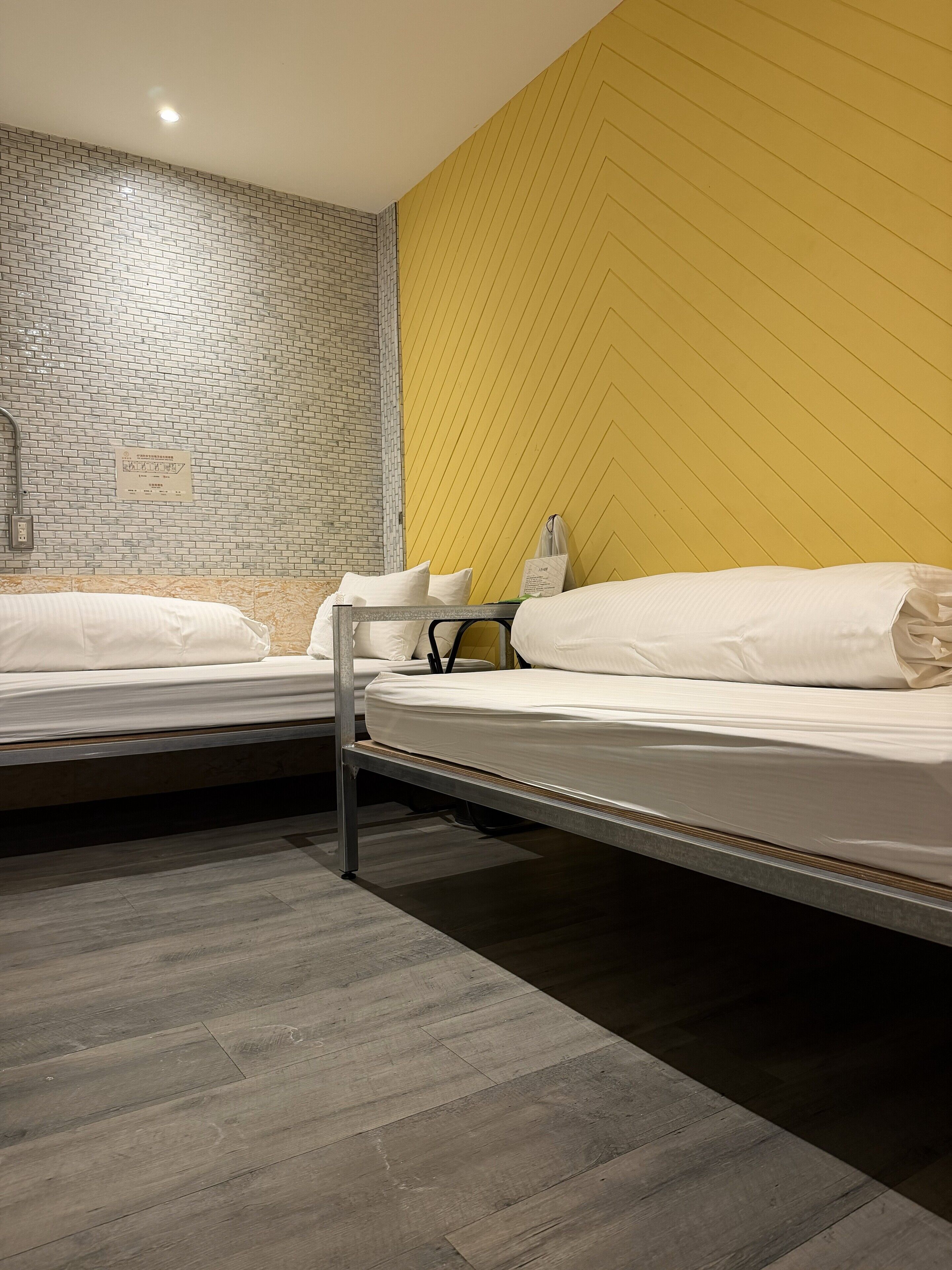 A hotel room with two beds, a brick-patterned wall, a yellow chevron wall, and a wooden floor.
