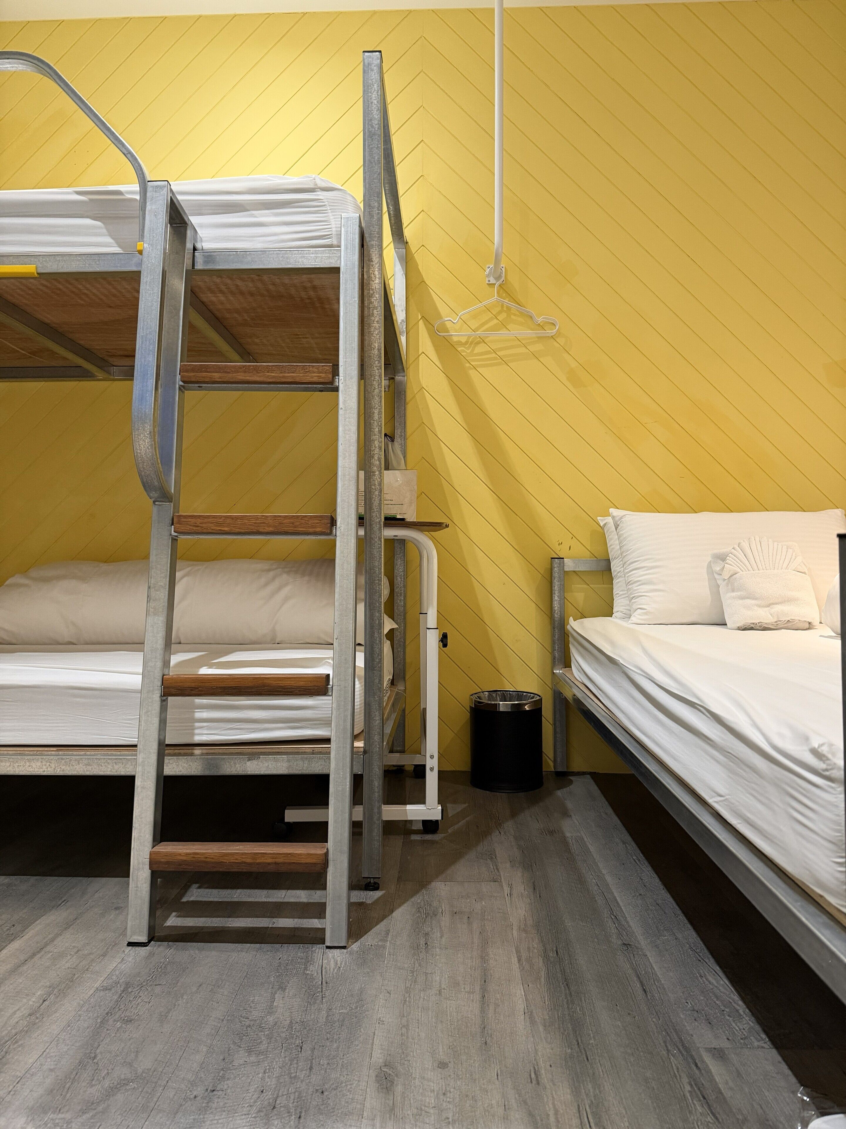 A bunk bed room with a metal ladder, a small trash bin, and a white hanging light fixture.
