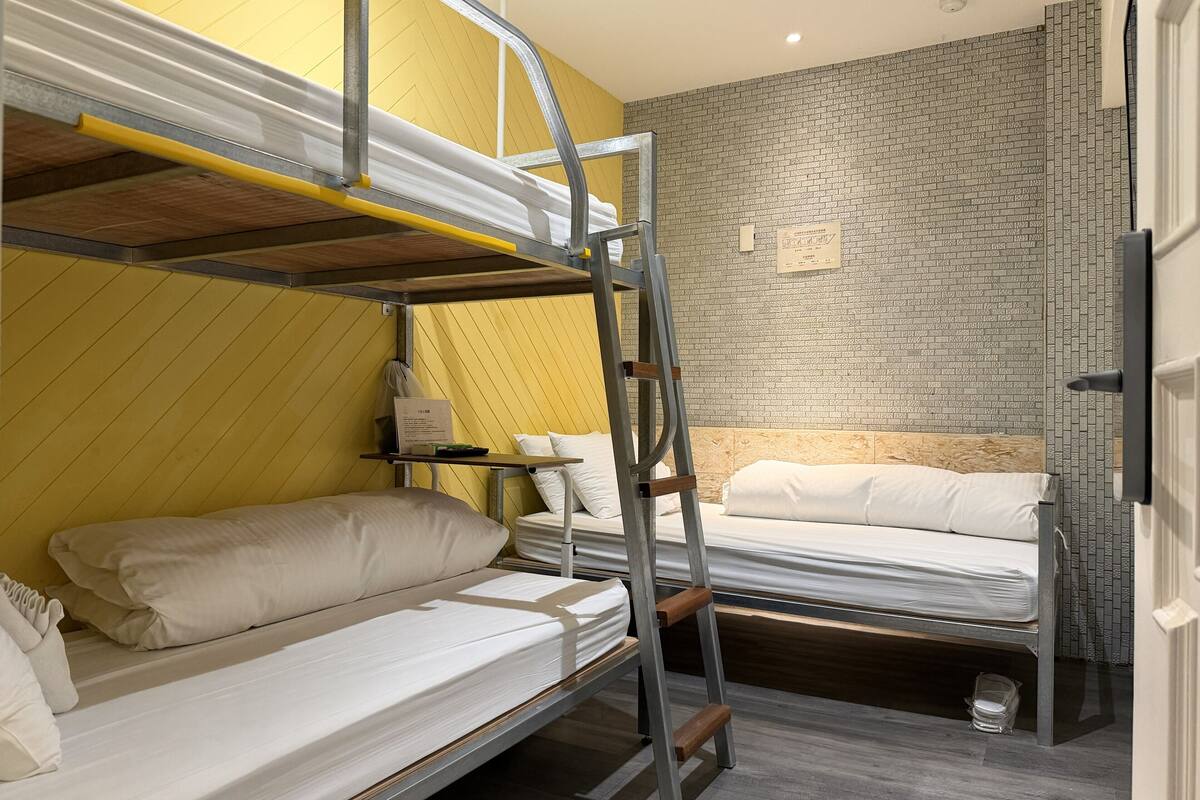 Quarto com beliche, uma mesinha pequena e parede com padrão de tijolos.