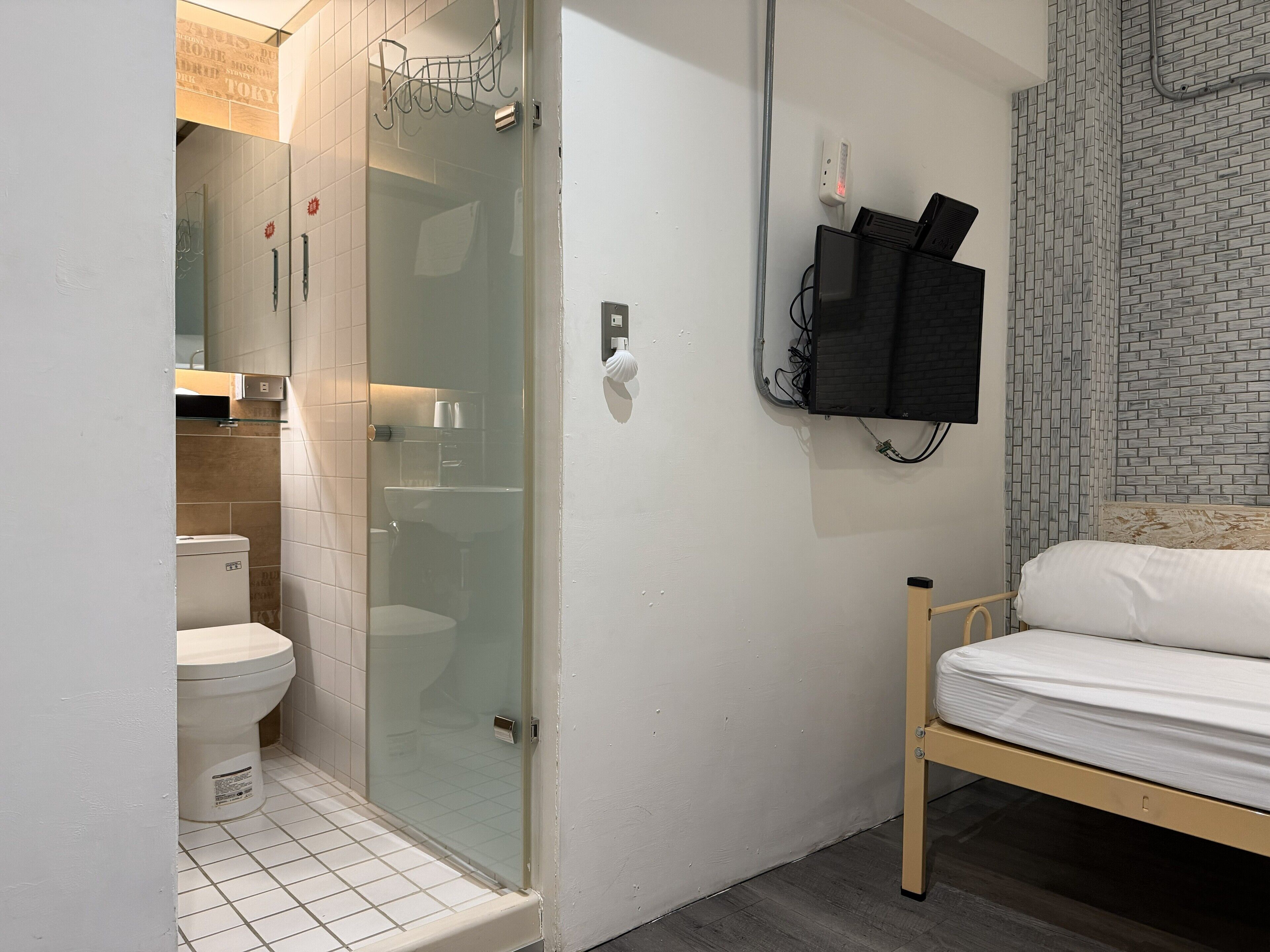A bathroom with a toilet, a glass-enclosed shower, and a bed with a white mattress.