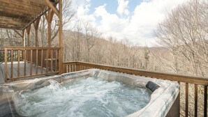 Een hottub op een houten terras, met uitzicht op een bebost gebied.