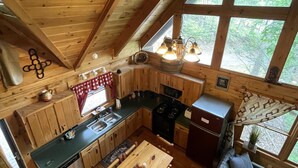 Un accogliente interno di una baita con finiture in legno, una zona pranzo, una cucina e ampie finestre che offrono vista sull'esterno.