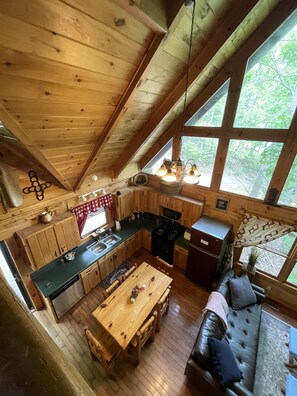 L’intérieur chaleureux d’un chalet, avec un décor en bois, un coin repas, une cuisine et de grandes fenêtres donnant sur le paysage extérieur.