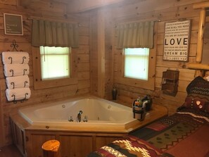 A cozy cabin-style room with a large bathtub, two windows with curtains, and a wall-mounted sign with motivational quotes. - Amazing Cabin! Easy Access! New Hot Tub! Close to all but secluded & private too (Sevierville)