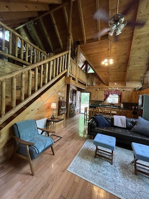 Une cabane en bois spacieuse, dotée d’un plafond haut, d’un escalier, d’un salon avec un canapé, une table basse et un tapis.
