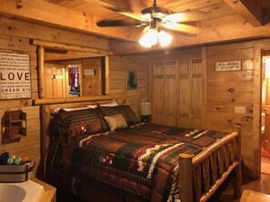 A wooden cabin-style room with a bed, a ceiling fan, and a wall with motivational quotes. - Amazing Cabin! Easy Access! New Hot Tub! Close to all but secluded & private too (Sevierville)