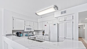 A modern kitchen with white cabinetry, a marble countertop, and stainless steel appliances. - Ocean Front Condo With Pool and Jacuzzi!!! (Oceanside)