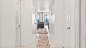 A hallway with white walls and doors, leading to a seating area with a view of the outdoors. - Ocean Front Condo With Pool and Jacuzzi!!! (Oceanside)