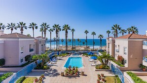 A resort with a swimming pool, palm trees, and a view of the ocean. - Ocean Front Condo With Pool and Jacuzzi!!! (Oceanside)