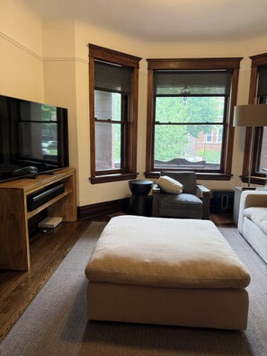 Ein Hotelzimmer mit großem Fenster, Flachbildfernseher, Sofa, Sessel und einer Holzunterhaltungsecke.