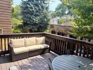 Une terrasse en bois avec un canapé en osier et une table en métal.