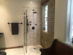 A modern bathroom with a glass-enclosed shower, a marble-tiled wall, a brick accent wall, and a window with a view. - The entire FLAT.  Stay Like You Own! Central AIR. TWO FULL BATHROOMS. Unique.  (Chicago)