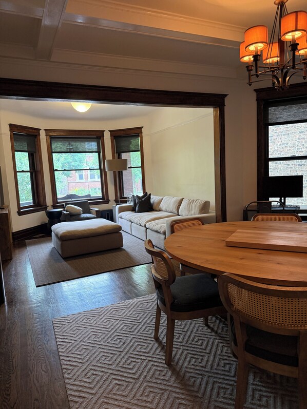 A living room with a sofa, ottoman, dining table, chairs, and a chandelier. - The entire FLAT.  Stay Like You Own! Central AIR. TWO FULL BATHROOMS. Unique.  (Chicago)