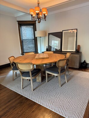 A dining area with a round wooden table, six chairs, a chandelier, and two large framed artworks on the wall. - The entire FLAT. Stay Like You Own! Central AIR. TWO FULL BATHROOMS. Unique. (Chicago)