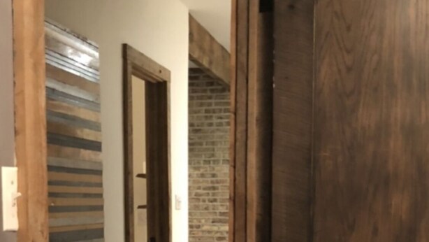 Un couloir avec un plancher en bois, une grande porte en bois et un mur de briques en arrière-plan.