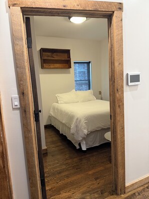 A bedroom with a wooden door frame, a bed with white bedding, a small window, and a wall-mounted light fixture. - The entire FLAT. Stay Like You Own! Central AIR. TWO FULL BATHROOMS. Unique. (Chicago)