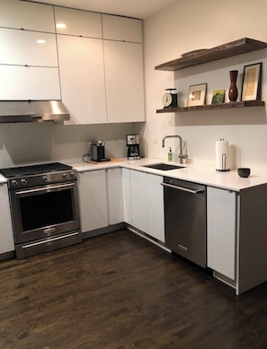A modern kitchen with stainless steel appliances, white cabinetry, and a wooden floor.