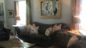A living room with a dark-colored sofa, a matching ottoman, and a coffee table. There is a painting on the wall and a lamp on a side table. - Gorgeous Private Countryside Getaway! (South Bend)