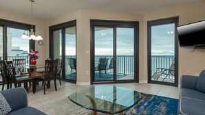 A spacious living room with a glass coffee table, a dining area with chairs, and a balcony with a view of the sea.