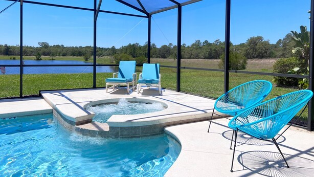 A pool area with a hot tub, two blue chairs, and a view of a lake.